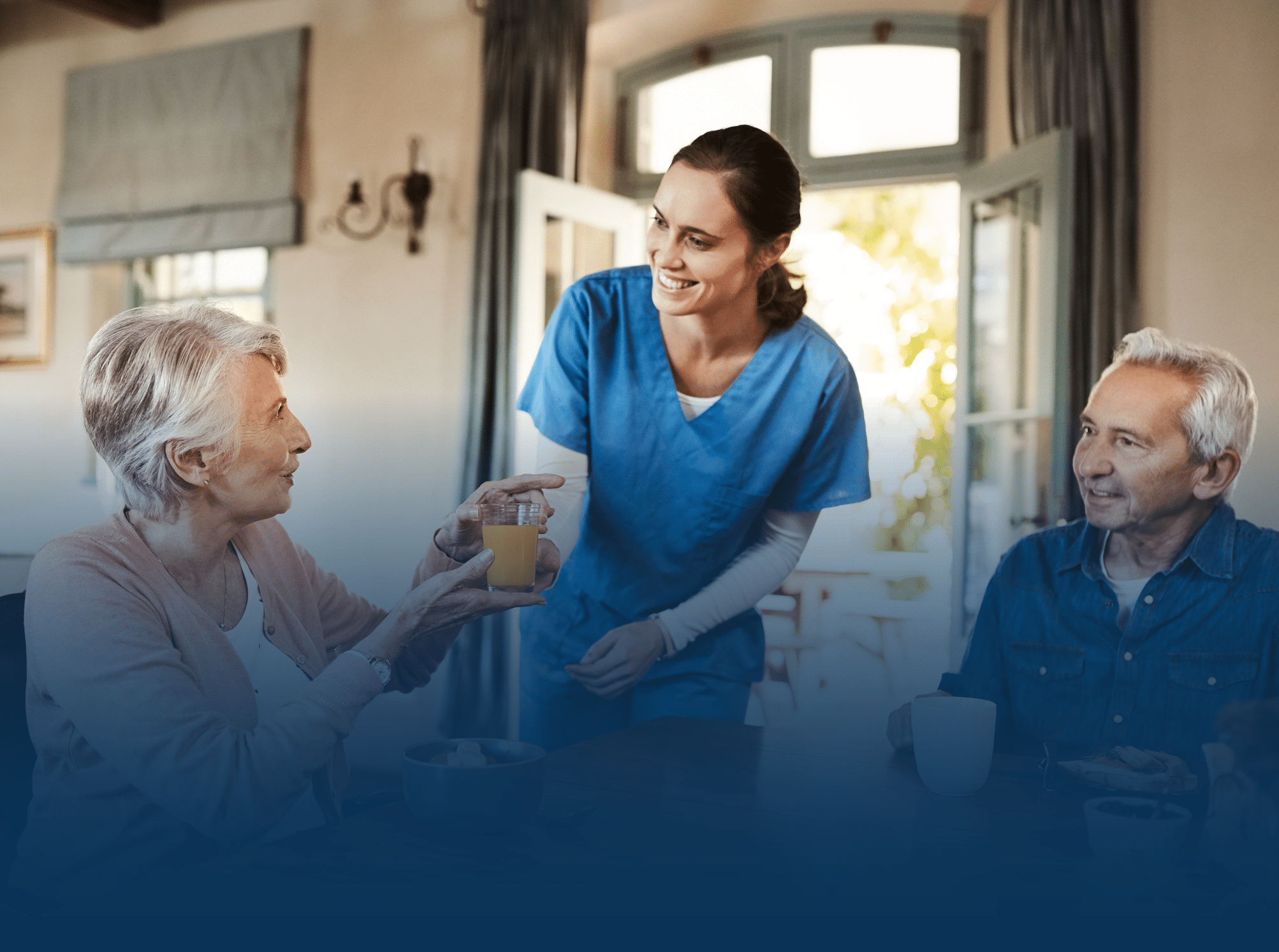 Woman in scrubs handing older woman orange juice at the breakfast table