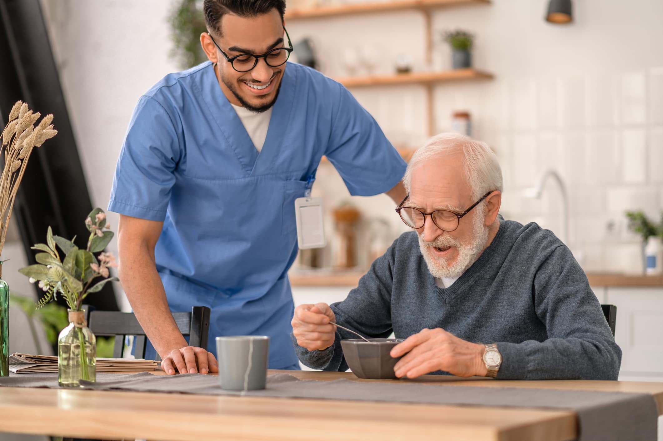 Smiling caregiver watching older man eat breakfast