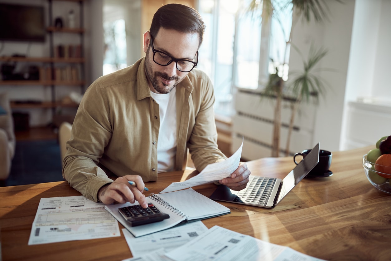 Young man using calculator while working on his financial plans at home.